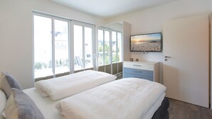 Un dormitorio con dos camas, televisión, baño y balcón con vistas.