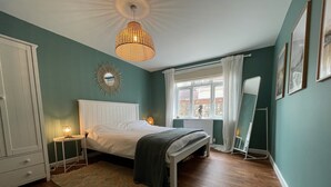 Et soveværelse med en seng, sengeborde med lamper, et spejl og et vindue med gardiner.