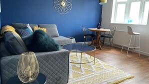 En stue med blå væg, et rundt bord og en sofa med et mønstret gulvtæppe.