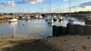 En lystbådehavn med flere sejlbåde i havnen, en stenet strand og en delvist overskyet himmel.