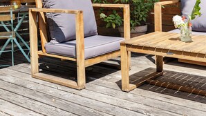 Une terrasse en bois avec deux chaises et une table, une clôture en bois et un pot de fleurs contenant des fleurs blanches.