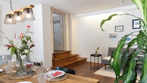 Un coin repas avec une table en bois dressée pour le repas, un escalier menant à une autre pièce et un espace de vie avec un canapé et une petite table d’appoint.