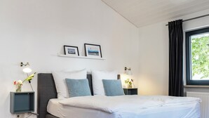 Une chambre moderne avec un grand lit, deux tables de chevet, une fenêtre avec des rideaux et un luminaire au plafond.