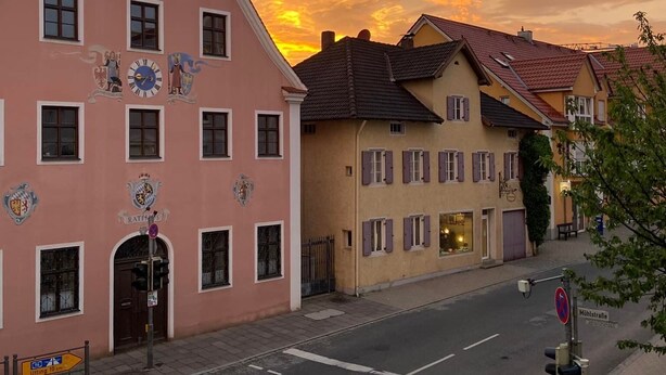 Une vue de rue présentant une architecture européenne traditionnelle, avec notamment un bâtiment rose orné d’éléments décoratifs et un bâtiment jaune avec des volets.