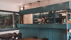 A bar area with a teal-colored counter, bar stools, and a view of the outdoors through a large window. - Woodland Chalet in the Ardennes (Olloy-sur-Viroin)