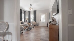 A spacious living room with a wooden floor, a sofa set, a coffee table, and a dining area.