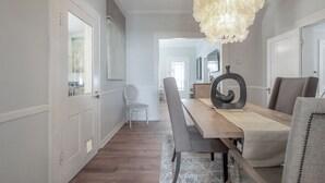 A dining area with a wooden table, grey upholstered chairs, a patterned rug, and a unique black decorative piece.