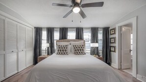 A bedroom with a large bed, a ceiling fan, and a view of the outside through the window.