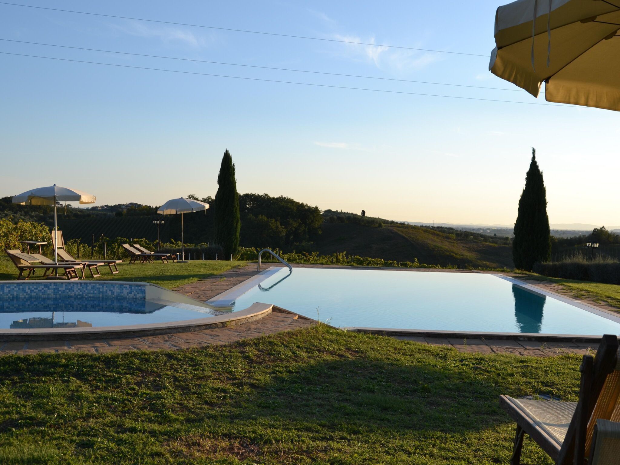 Une piscine entourée de pelouse et d’arbres, avec des chaises longues et des parasols.