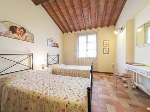 Un dormitorio con dos camas individuales, techo de madera, una ventana con cortinas, un escritorio con silla y obras de arte en las paredes.