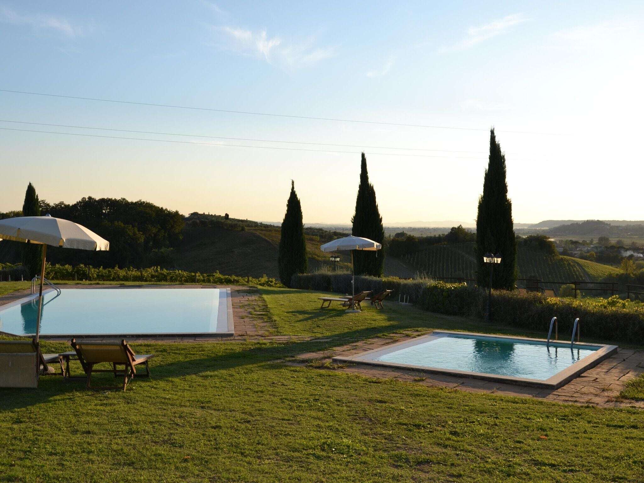 Un área de piscina con dos piscinas, sillas de descanso y sombrillas.
