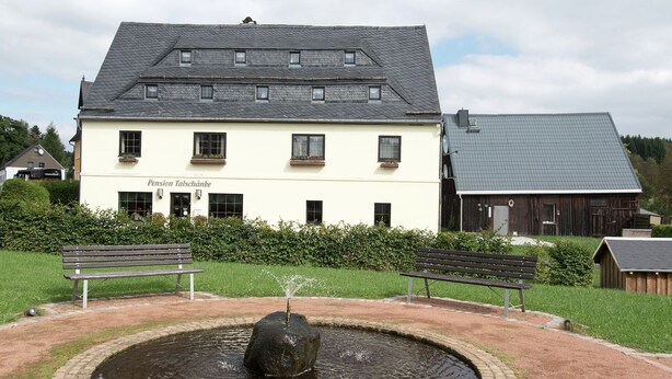 Een gebouw met een bord waarop 'Pension Talschänke' staat en een fontein met een rots in het midden.