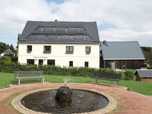 En bygning med et skilt der viser "Pension Talschänke" og en cirkulær springvand med en sten i midten.