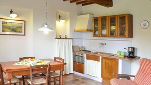 A cozy kitchen with wooden cabinets, a dining table with chairs, and a striped chair. - Belvilla by OYO Geranio (Stabbia)