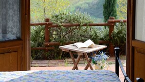 A room with a wooden balcony, a small table with an open book, and a view of a green landscape. - Belvilla by OYO Geranio (Stabbia)