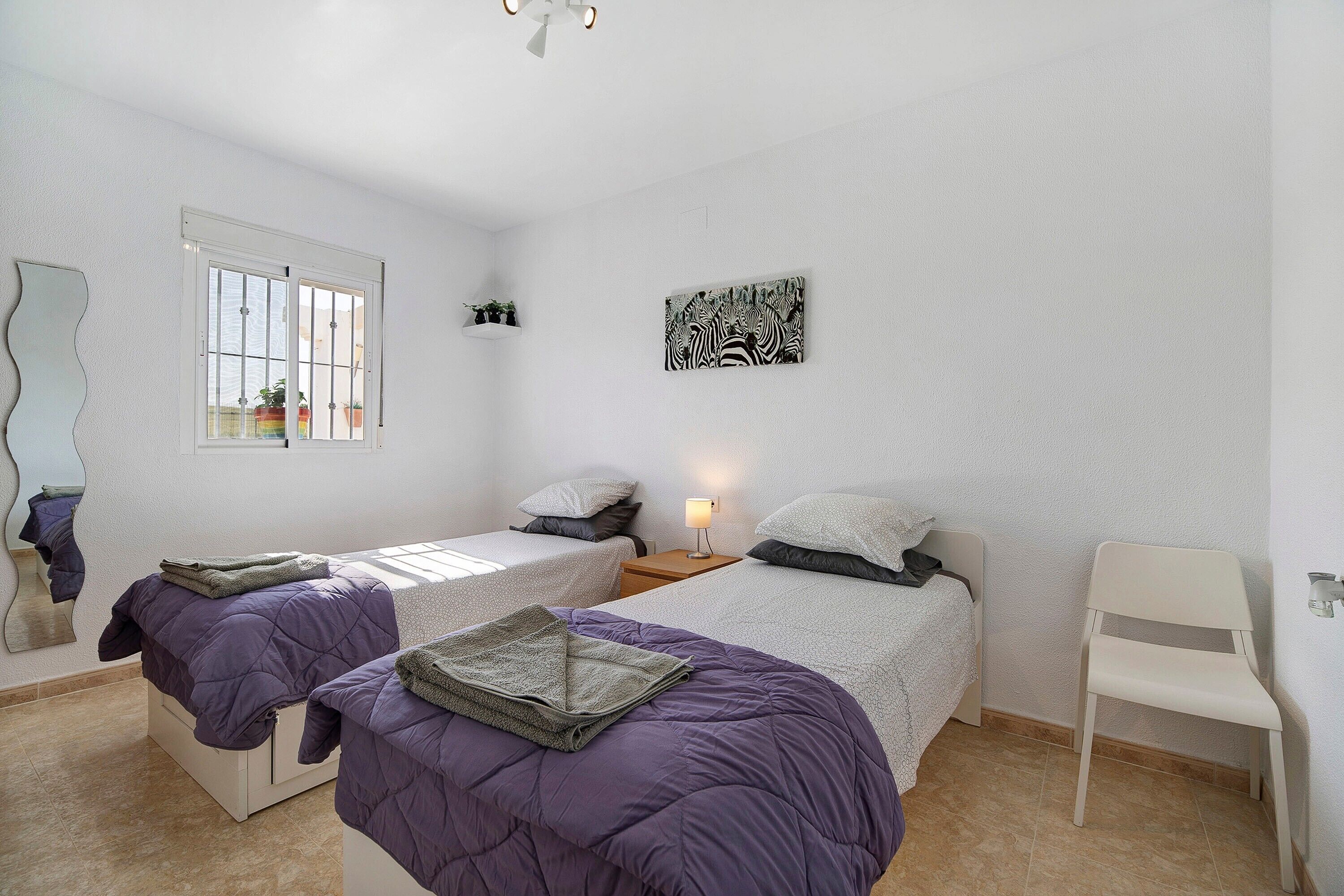 Een slaapkamer met twee bedden, een raam, een zwart-wit zebra afbeelding en een stoel.