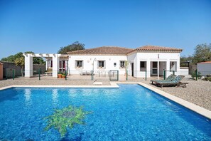 A swimming pool with a clear blue water feature, a white building with a tiled roof, and a covered patio area. - Villa Sol Country House with Mountain Views, Wi-Fi, and Air Conditioning (Chiclana de la Frontera)