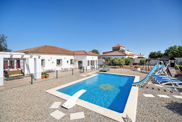 Una piscina con tobogán, un patio amurallado y un edificio con tejado de baldosas.