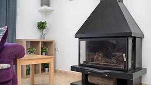 Un salon moderne avec un poêle à bois noir, une table en bois et un fauteuil violet.