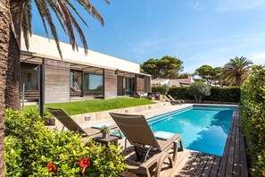Un área moderna junto a la piscina con sillas de descanso, una piscina e un jardín bien cuidado.