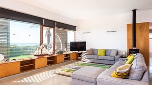 Een moderne woonkamer met een groot raam, een flatscreen-tv, een grijze bank en een houten entertainmentkast.