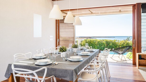 Een eetgedeelte met een tafel gedekt voor vier personen, witte stoelen en uitzicht op zee.