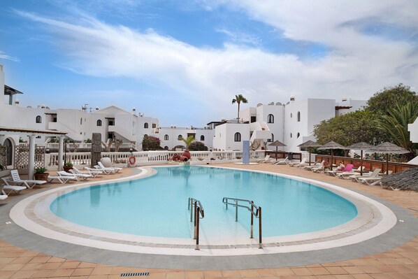 Une piscine entourée de bâtiments blancs, de chaises longues et de parasols.