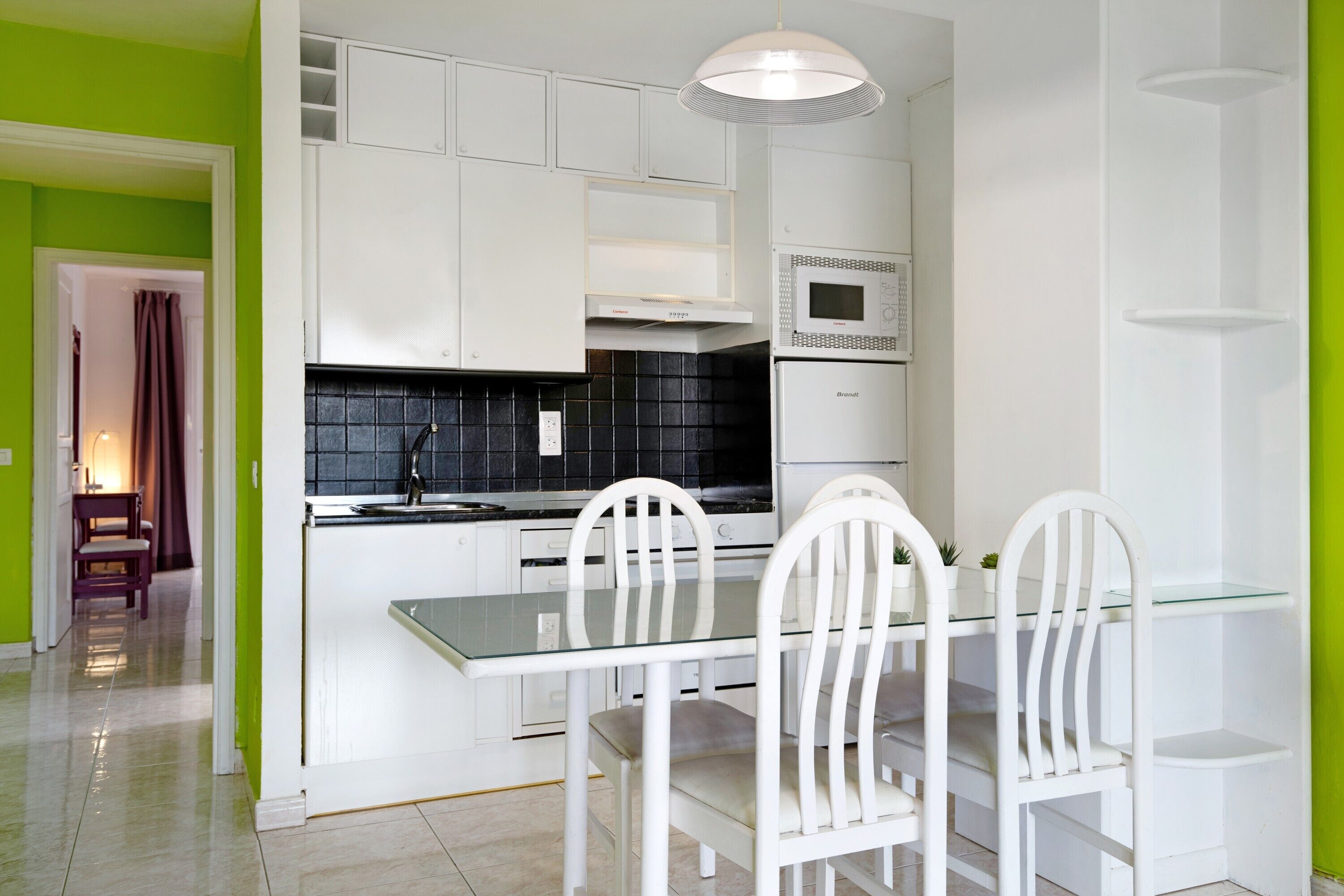 Una cocina moderna con armarios blancos, un salpicadero de baldosas negras y una mesa de comedor de vidrio con sillas blancas.