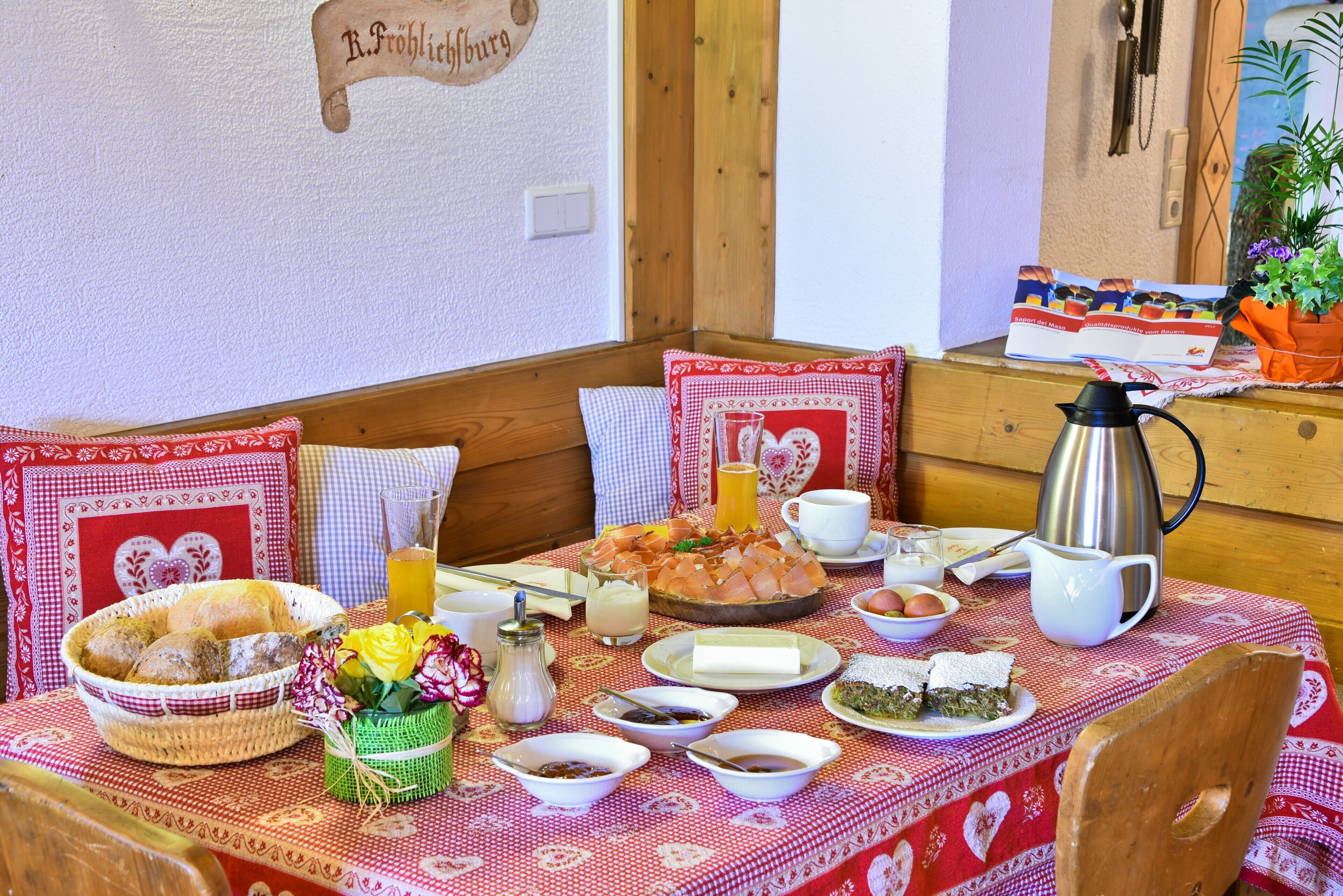 Une table à manger dressée avec différents plats, un panier de pain et une cafetière.