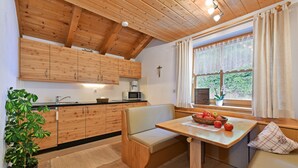 Eine Küche mit Holzausstattung, einer Sitzbank, einem Tisch mit Obst und einem Fenster mit Vorhängen.