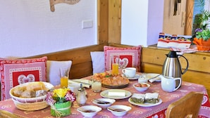 Una mesa de comedor dispuesta con diferentes platos, una cesta de pan y una cafetera.