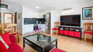 Un salón moderno con una mesa de centro de vidrio, sofá rojo y un televisor sobre un mueble negro.