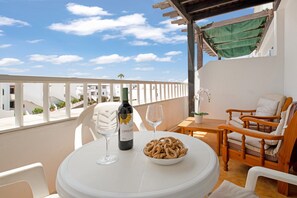 Un balcon avec une table, des chaises, une bouteille de vin et un bol de collations.