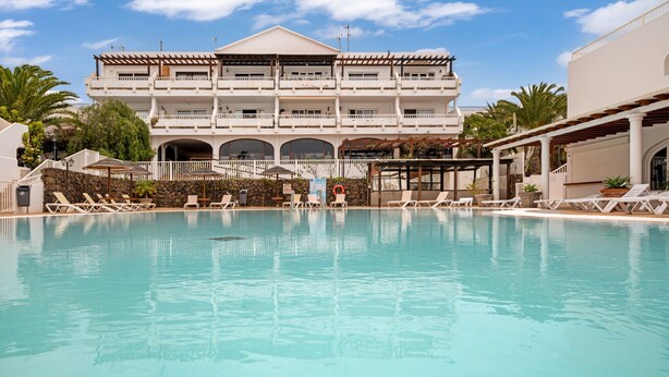 Un hotel con piscina, varios balcones y una pared de piedra.