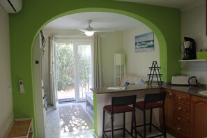 A kitchen with a green archway, a ceiling fan, a coffee maker, and a bar area with two stools.