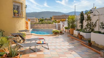 Un área junto a la piscina con sillones de descanso, una piscina pequeña y plantas en macetas.