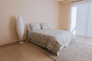 A bedroom with a bed, a standing lamp, and a large window.