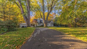 Ein Wohnhof führt zu einem Haus, umgeben von Bäumen mit Herbstlaub.