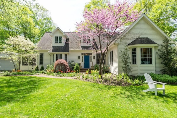 A two-story house with a front porch, a blue door, and a garden with a lawn and flowering plants.