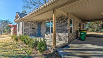 A brick house with a covered porch, a front door, and a green trash bin.