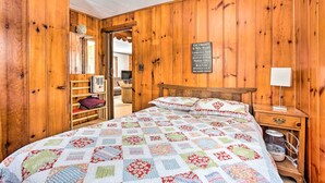 A wooden-paneled room with a bed, a nightstand, a lamp, and a sign listing nearby locations. - Remote Michigan Retreat on 10 Acres w/ Grill! (Wellston)