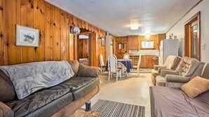 A cozy living room with a brown leather sofa, a beige armchair, and a dining area with a table and chairs. - Remote Michigan Retreat on 10 Acres w/ Grill! (Wellston)