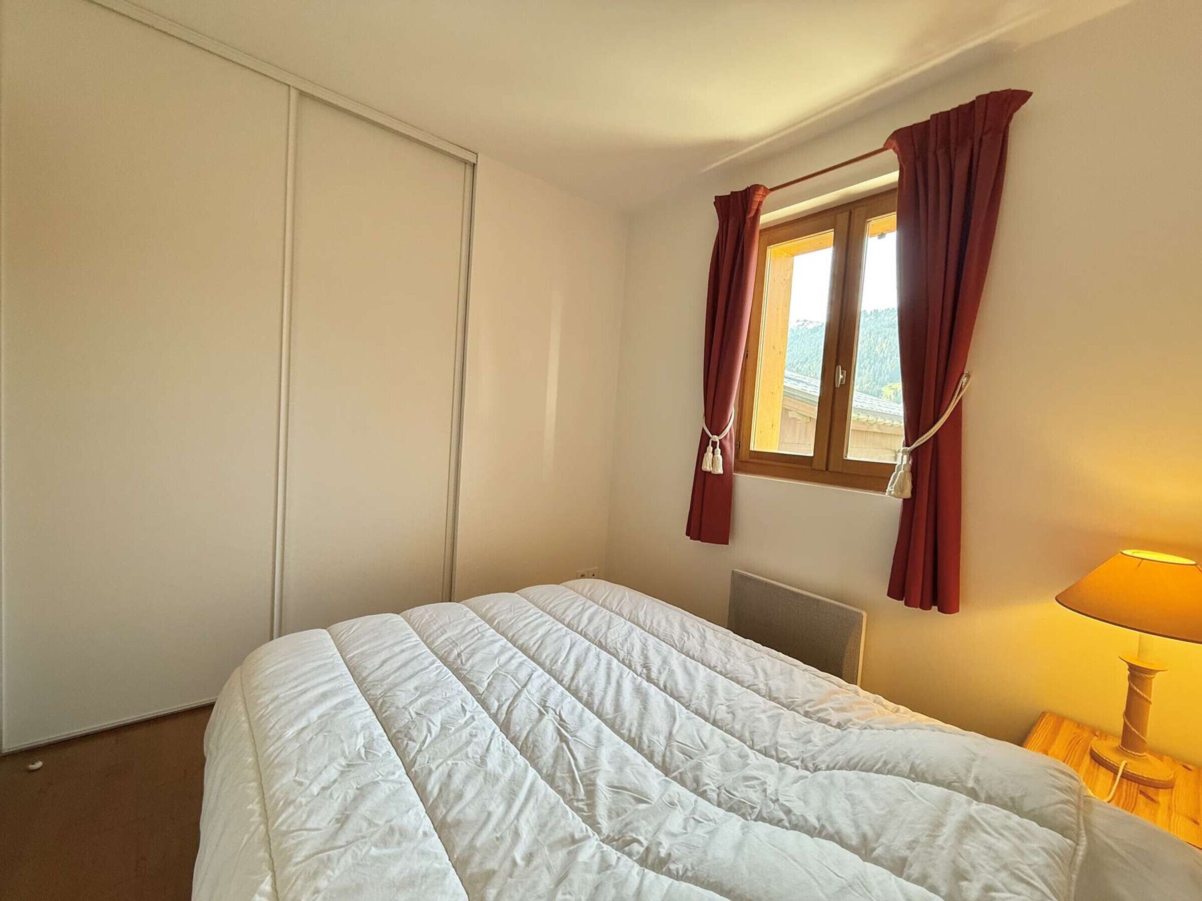A bedroom with a bed, a window with curtains, a radiator, and a lamp.