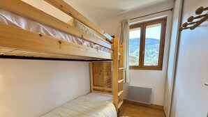 A bunk bed room with a window, wooden walls, and a radiator. - Spacious 3-Room Apartment in Praz-Sur-Arly, Sleeps 6, Central Location, Parking Included (Praz-sur-Arly)