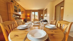 A wooden dining table set for six with white plates and glasses, surrounded by wooden chairs. - Spacious 3-Room Apartment in Praz-Sur-Arly, Sleeps 6, Central Location, Parking Included (Praz-sur-Arly)