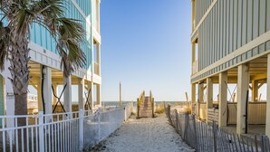 A sandy pathway leading to a wooden staircase, flanked by white fences and palm trees, with a clear sky above. - REEL RETREAT-LAGOON FRONT PRIVATE COTTAGE, EXTRA AMENTIES, BEACH ACCESS, LOTS OF OUTDOOR FURNITURE (Gulf Shores)