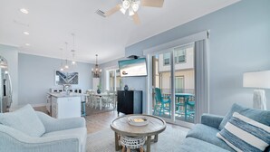 A spacious living room with a round coffee table, light blue sofas, and a television mounted on the wall. - REEL RETREAT-LAGOON FRONT PRIVATE COTTAGE, EXTRA AMENTIES, BEACH ACCESS, LOTS OF OUTDOOR FURNITURE (Gulf Shores)