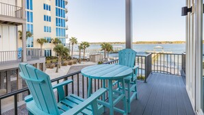 A balcony with turquoise Adirondack chairs and a small table, overlooking a body of water with a dock and a gazebo. - REEL RETREAT-LAGOON FRONT PRIVATE COTTAGE, EXTRA AMENTIES, BEACH ACCESS, LOTS OF OUTDOOR FURNITURE (Gulf Shores)