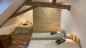 A cozy attic bedroom with two beds, exposed wooden beams, and a stone wall. - Charming XIXth Century Château near Le Mans with Pool and Park (Parennes)
