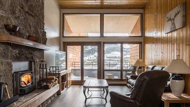 A cozy living room with a stone fireplace, a comfortable leather chair, a wooden coffee table, and large windows offering a view of the outdoors.